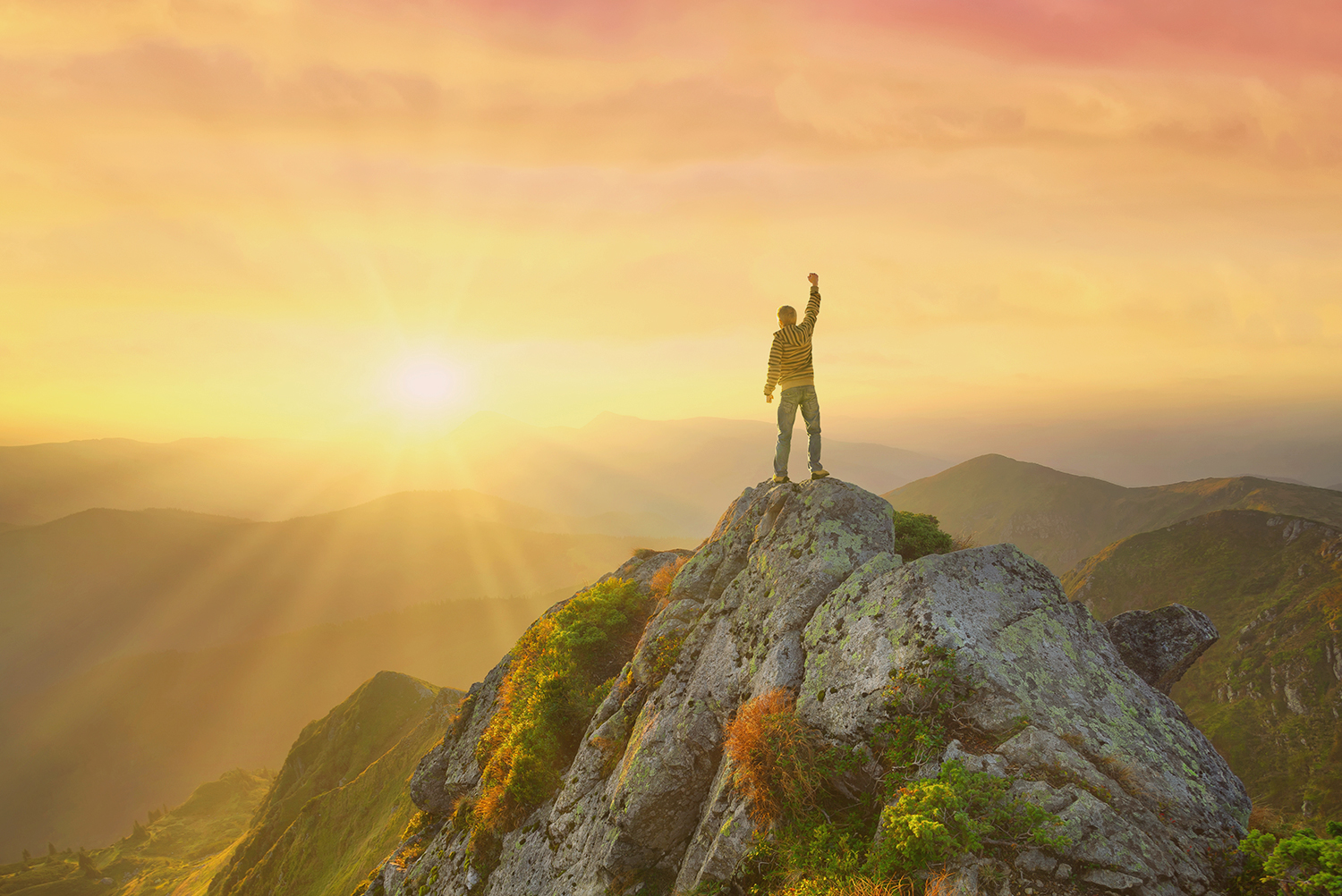 Person standing triumphantly on a mountain peak at sunrise, symbolising project ambition and impact