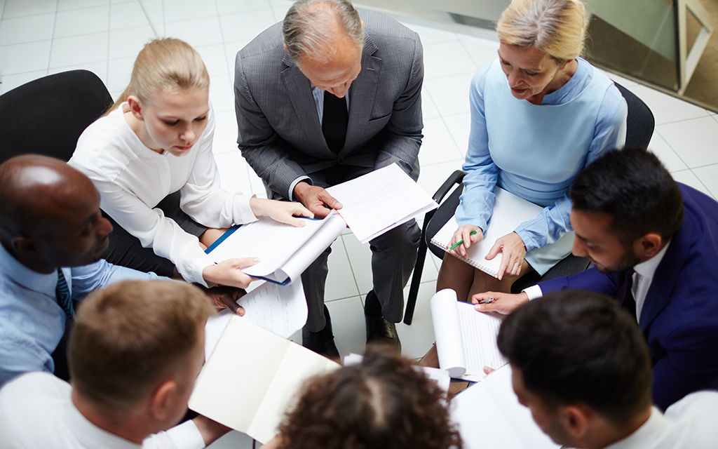 Business team in a group meeting, seated in a circle and reviewing printed documents together.